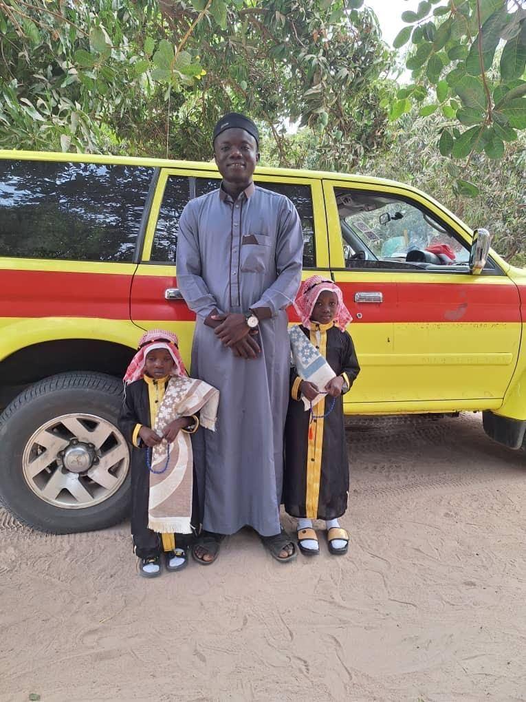 Ein Mann mit zwei Kindern aus der Gemeinde Buniadu, festlich gekleidet, vor dem Rettungsfahrzeug.